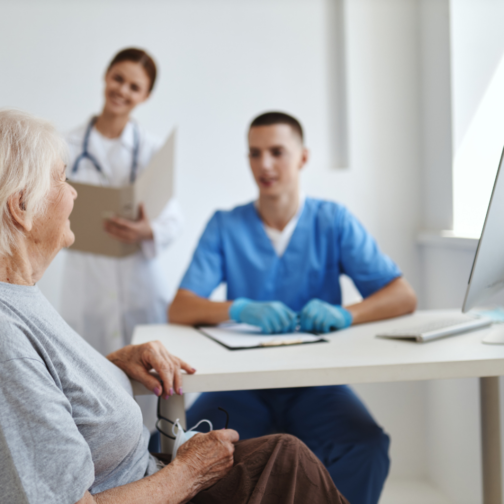 A doctor together with a nurse interacting with an elderly person, while in the background a screen